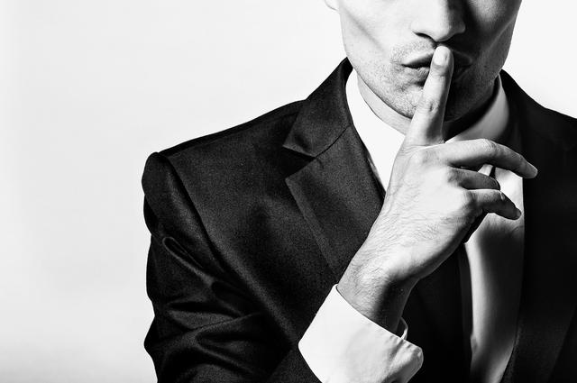 Person in suit making "shush" gesture