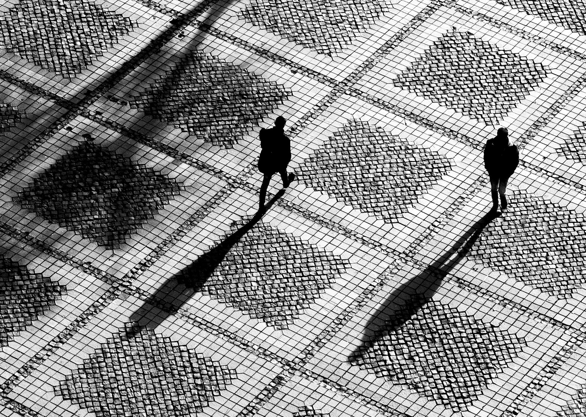 black and white birds eye view of two people walking past each other on outdoor tiled path