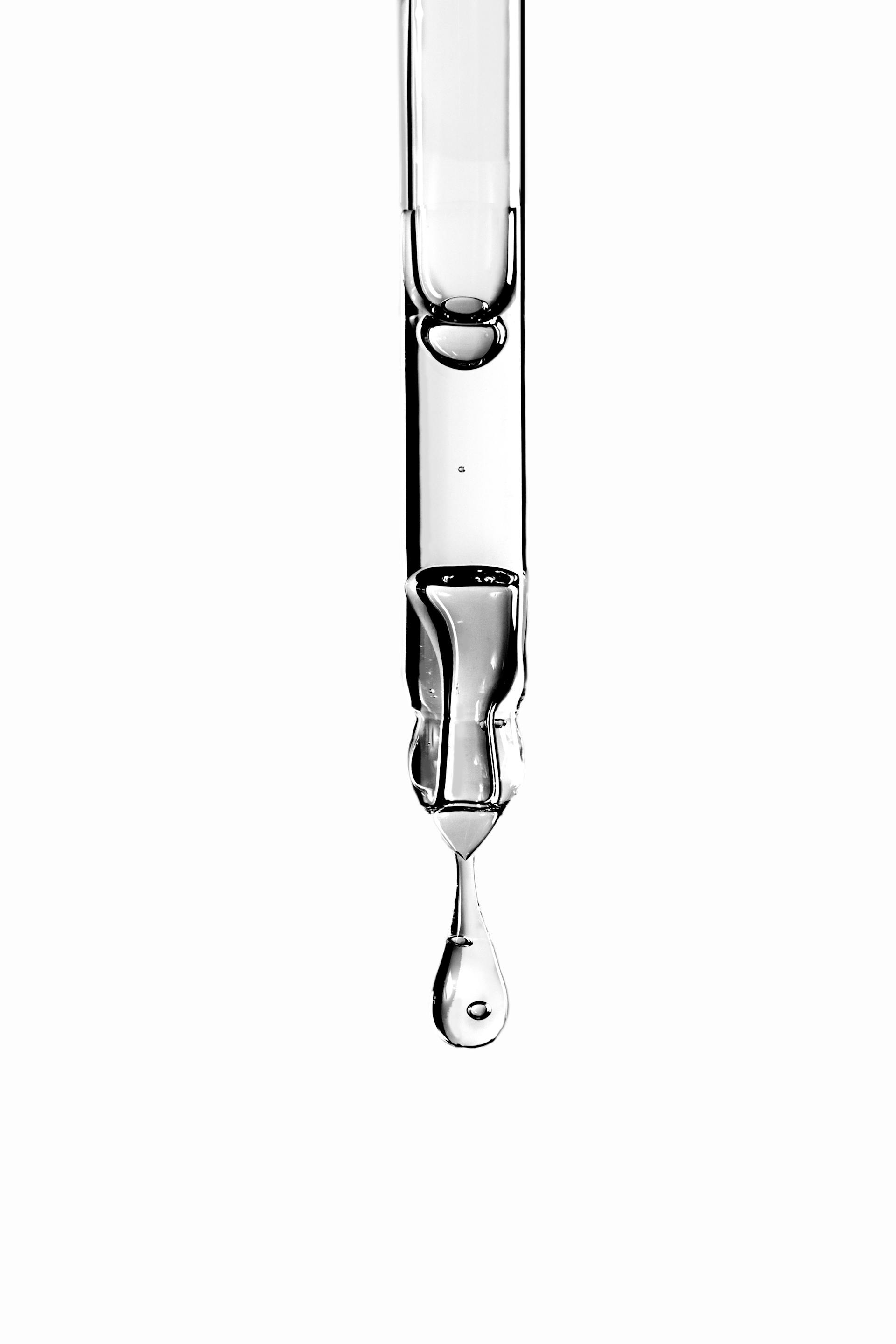 Close up of a glass syringe with one drop of clear liquid emerging from the dropper at the bottom