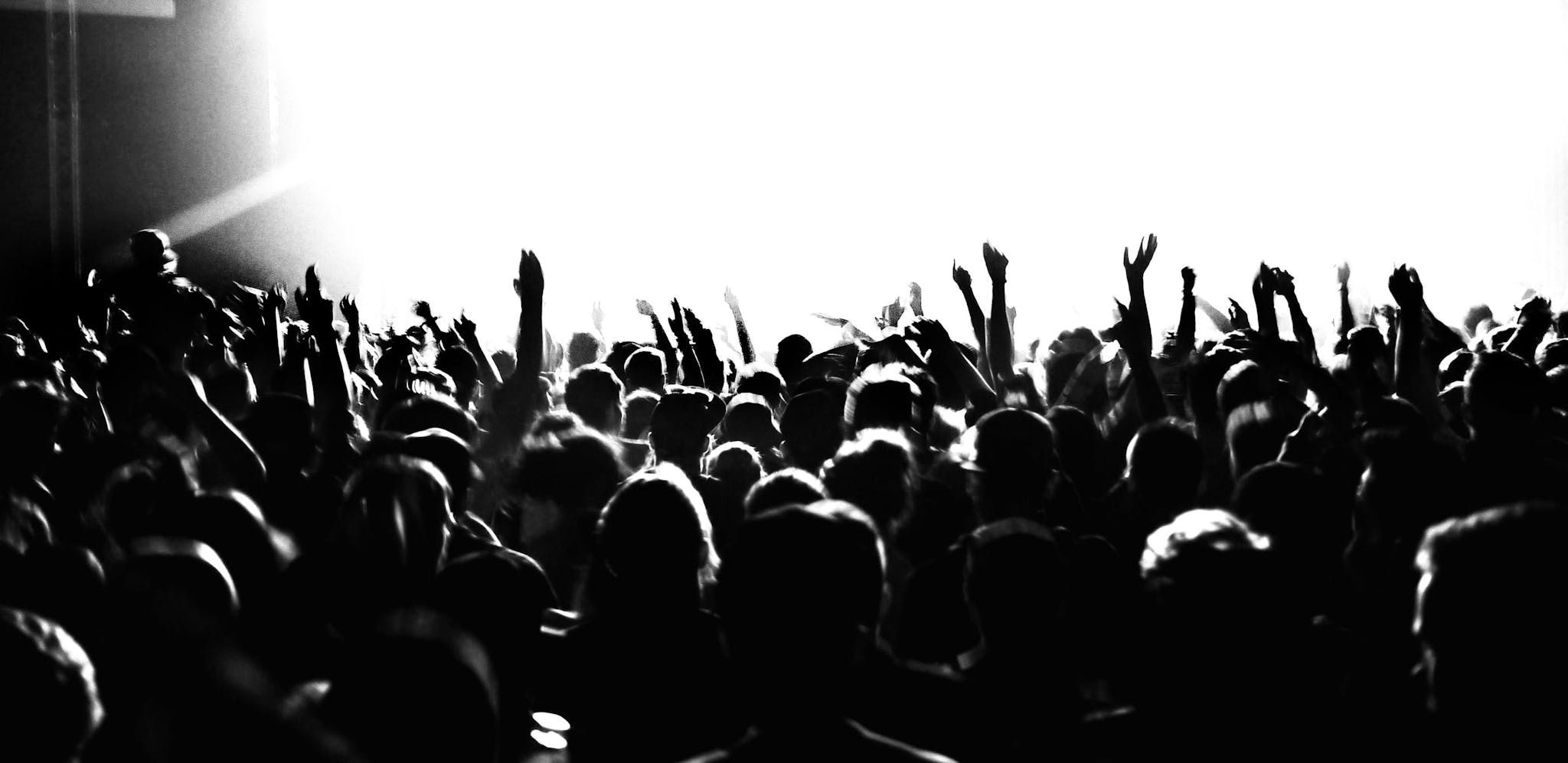 Black and white image of a crowd of people standing, cheering, and dancing at an event