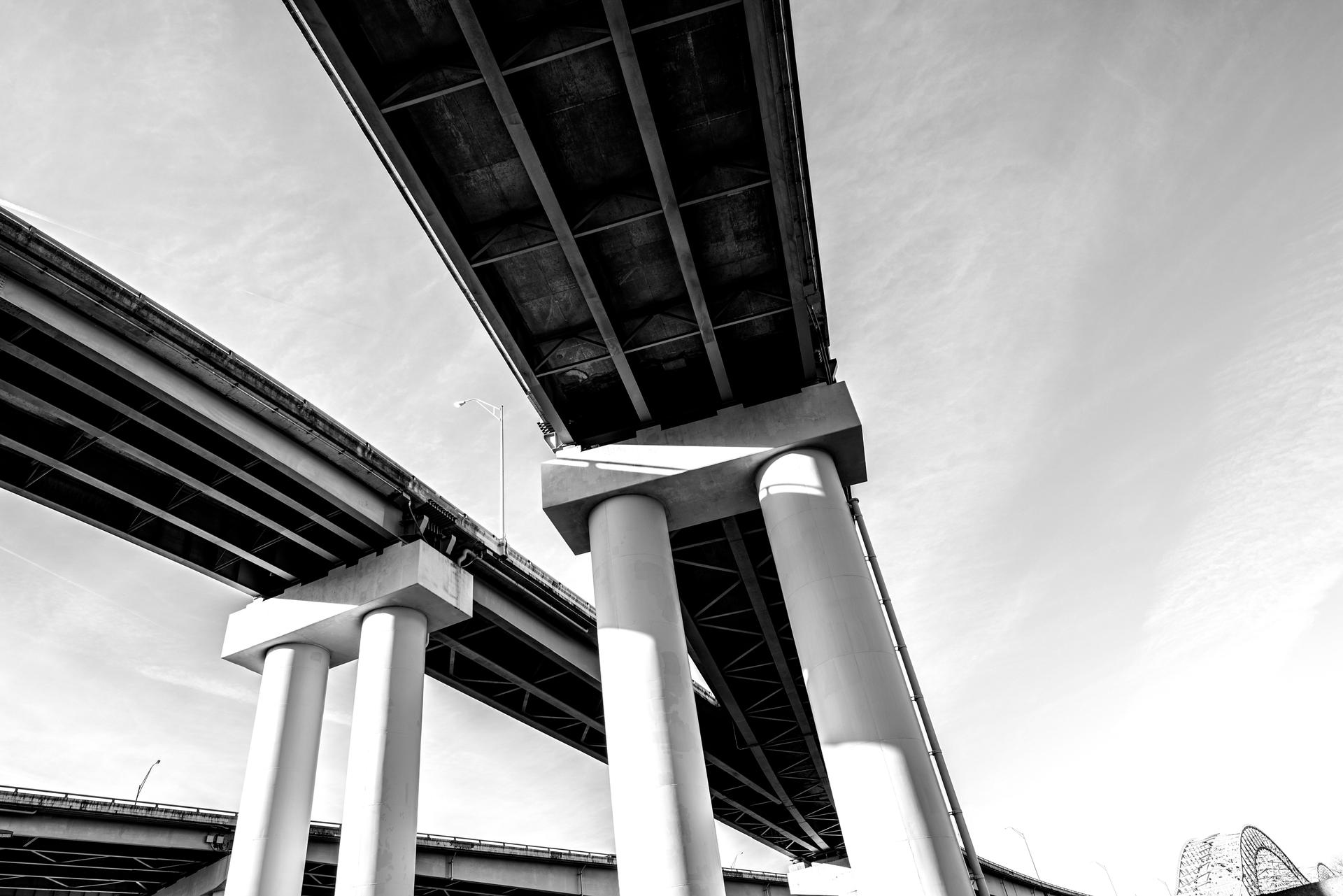 Photo looking up at the pillars supporting a road leading towards a bridge