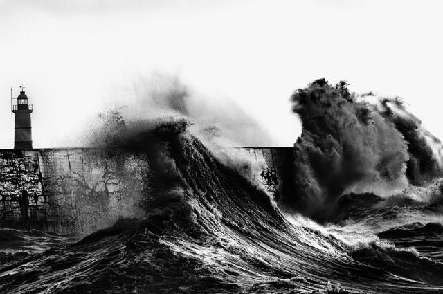 Waves crashing on a pier with lighthouse in the middle left