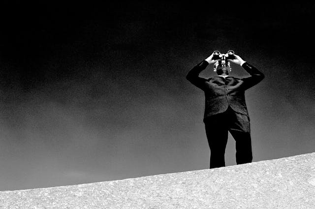 Man in suit looks through binoculars