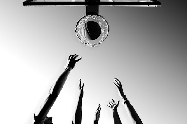 Hands reaching up towards a basketball falling through the hoop